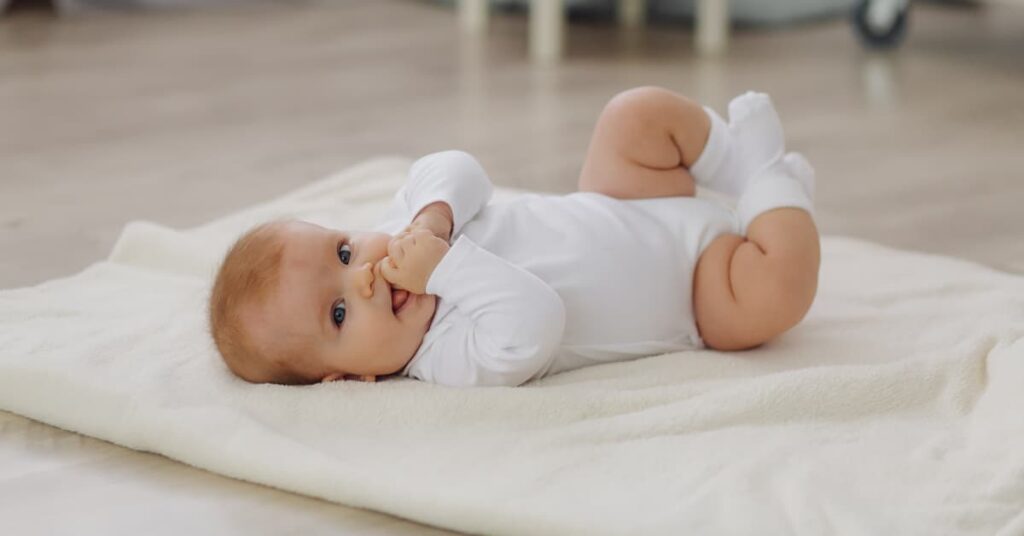 Bebé tumbado sobre una manta blanca, tranquilo y sonriente, imagen representativa del frenillo lingual en bebés.